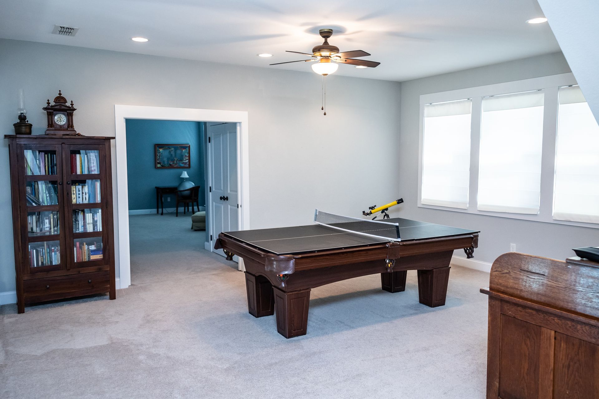A billiards table with a table tennis conversion top sits in a gray room featuring a bookshelf and a view into a study.