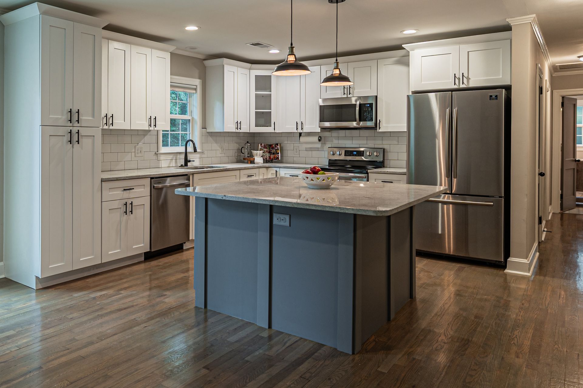 A modern kitchen featuring white cabinets, stainless steel appliances, a grey center island, and wood flooring.