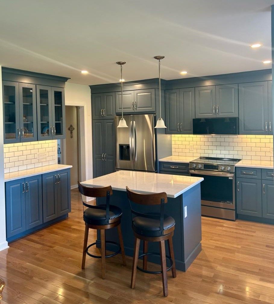 A modern kitchen with dark blue cabinets, white countertops, a center island with two bar stools, and hardwood floors.