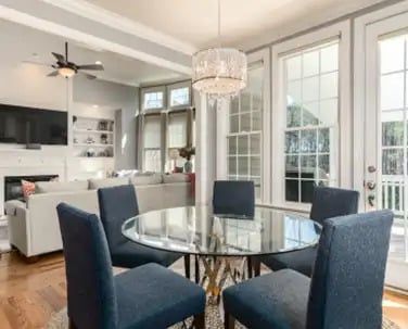 A dining area with a glass-topped table and four navy blue chairs, adjacent to a bright living room with a couch and TV.