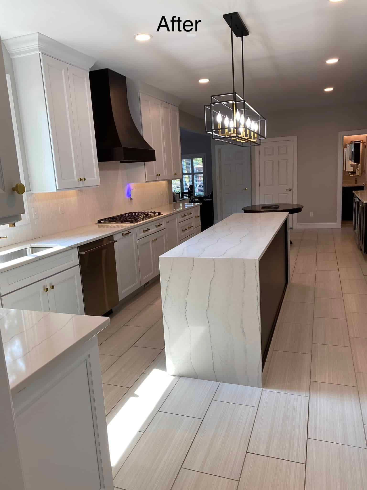 A modern white kitchen featuring an island, black vent hood, and pendant lighting over a polished floor.