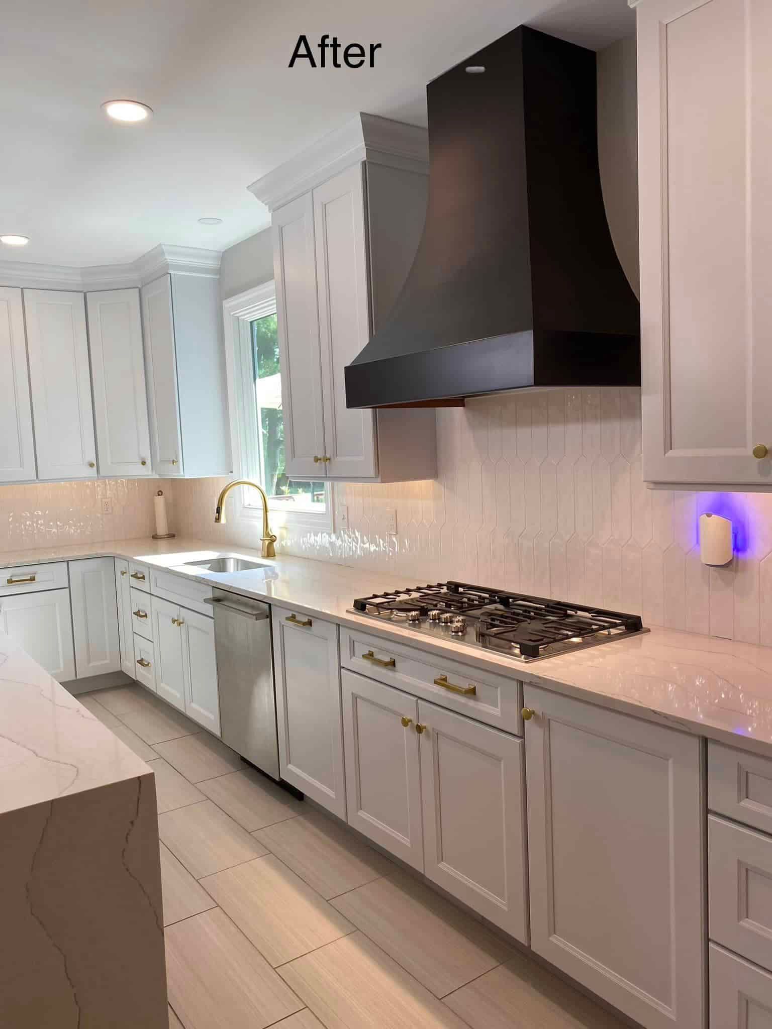 A modern kitchen featuring white cabinets, a large black range hood, stainless steel appliances, and quartz countertops.