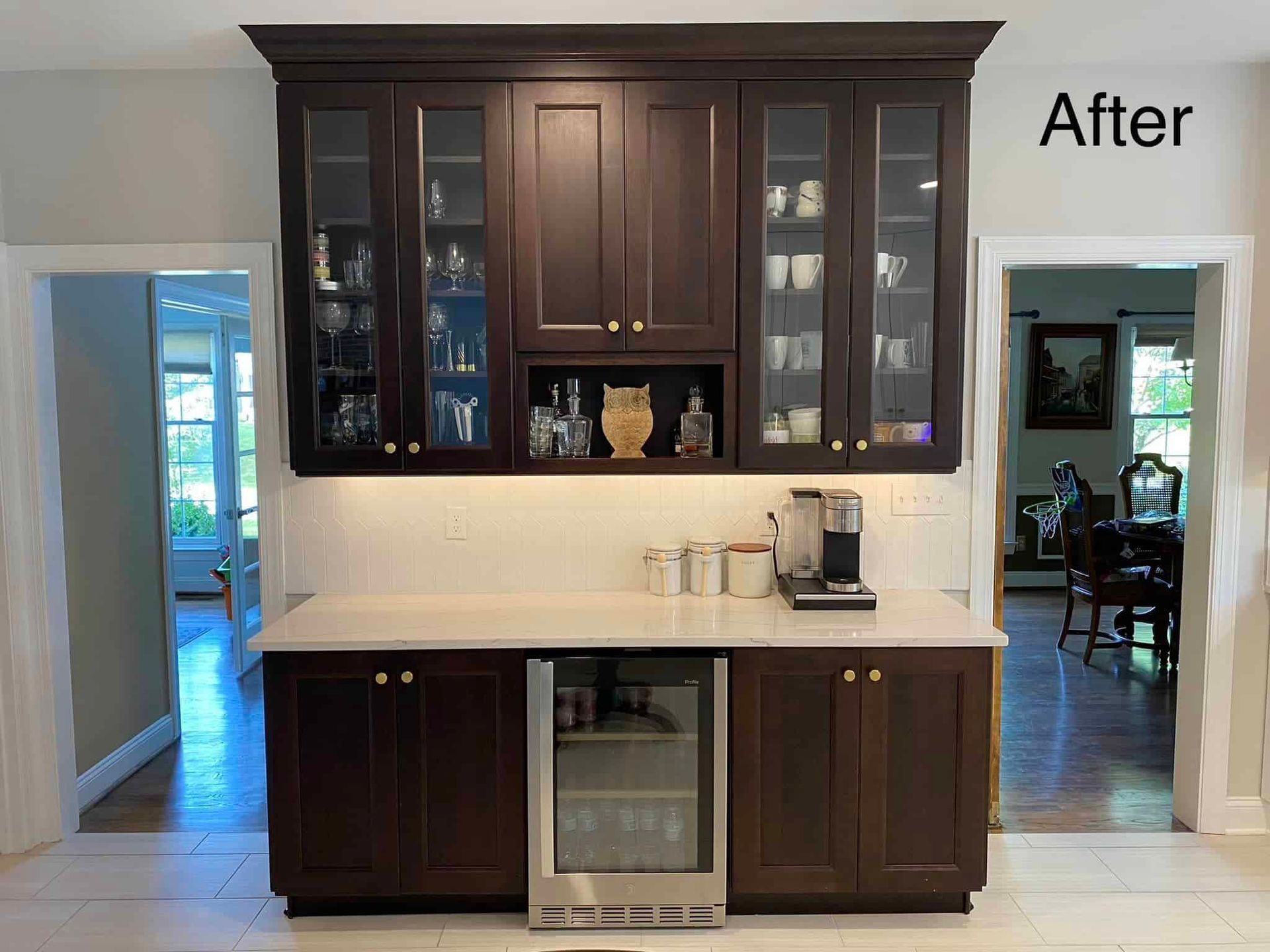 A wet bar featuring dark wood cabinets, glass-front upper displays, a central wine cooler, and light-colored countertops.
