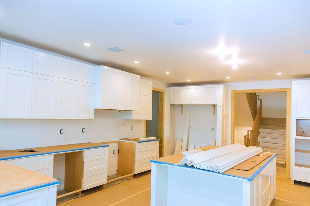 A kitchen under construction featuring white cabinets, unfinished wooden countertops, and an island in a bright room.
