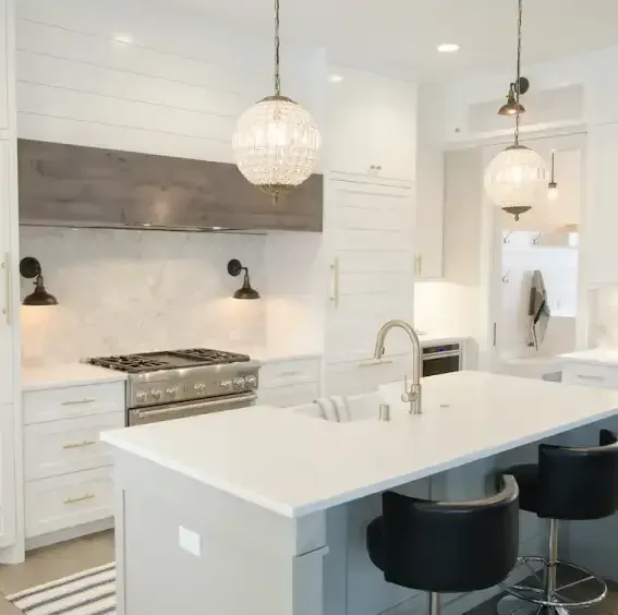 A bright, modern kitchen featuring a white island with black stools, white cabinets, and a grey wood range hood.