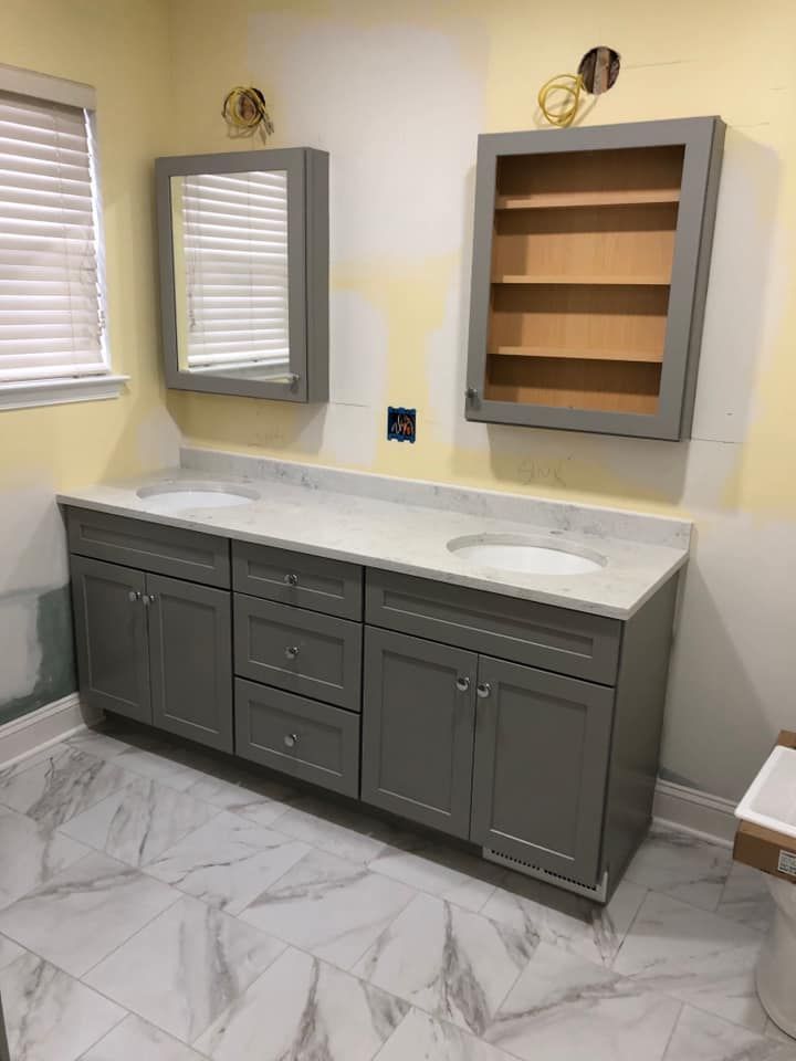 A bathroom vanity with grey cabinets, white marble countertop, two undermount sinks, and two matching grey medicine cabinets.