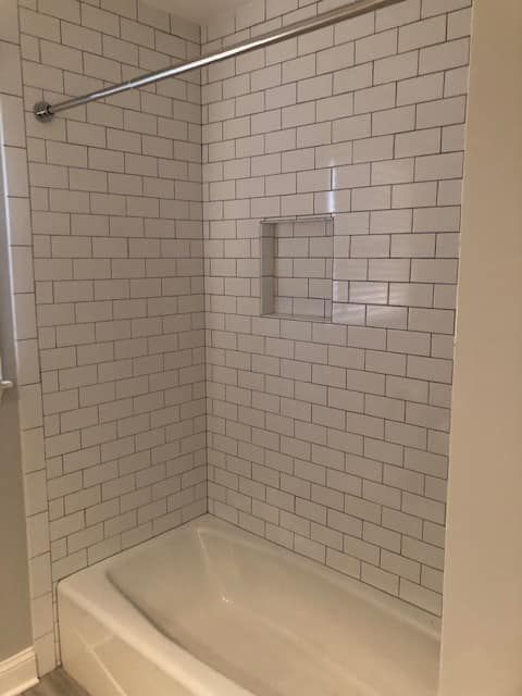 A white subway-tiled bathtub alcove with a built-in recessed shelf and a metal shower curtain rod.