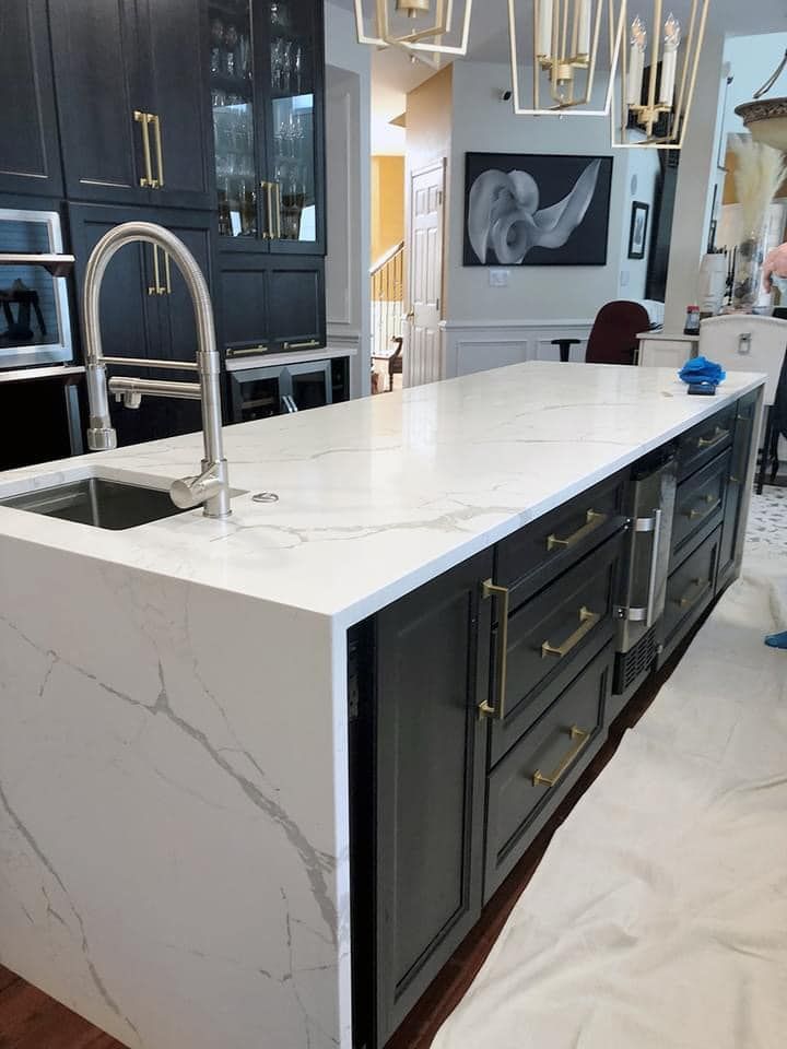 A kitchen island featuring a white marble countertop with gray veining and dark navy cabinetry, captured from an angle.