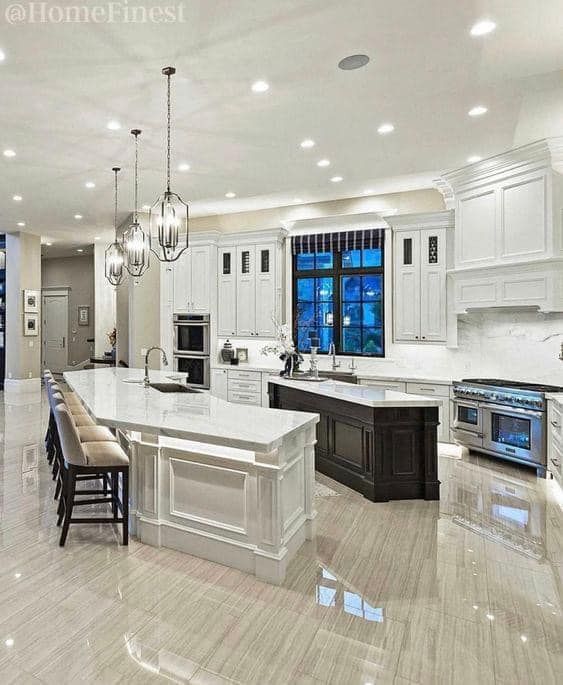 A spacious, modern kitchen featuring white cabinets, a large white countertop island with seating, and a dark wood island.