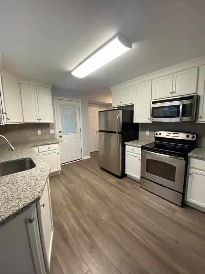 A modern, well-lit kitchen with white cabinets, granite countertops, stainless steel appliances, and wood-look flooring.