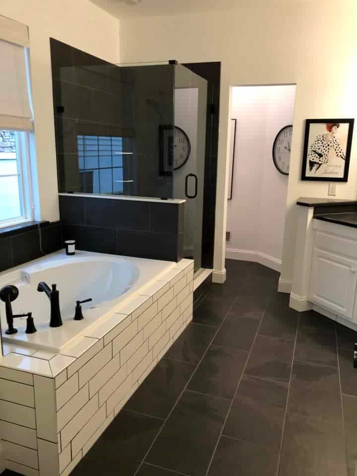 A bathroom featuring a white soaking tub, a dark-tiled walk-in shower, dark tile floors, and a framed wall art piece.