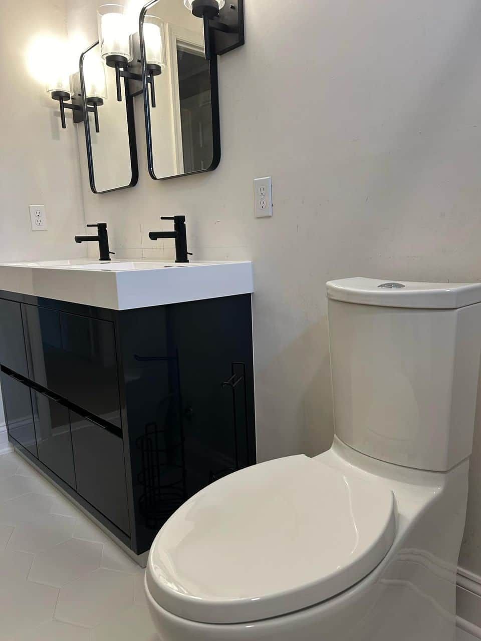 A modern bathroom vanity with dual black faucets, two rectangular mirrors, and a white toilet.