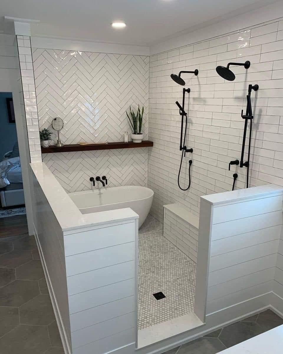 A modern bathroom featuring a white soaking tub, a double shower with black fixtures, and white herringbone tiled walls.