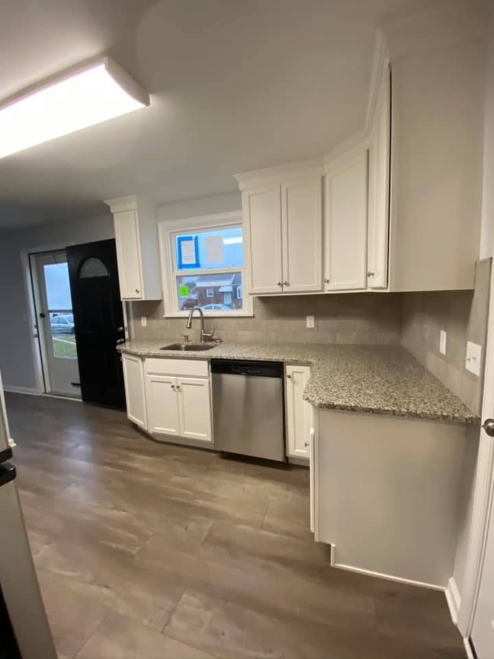 A bright kitchen featuring white cabinets, granite countertops, wood-look flooring, and a stainless steel dishwasher.