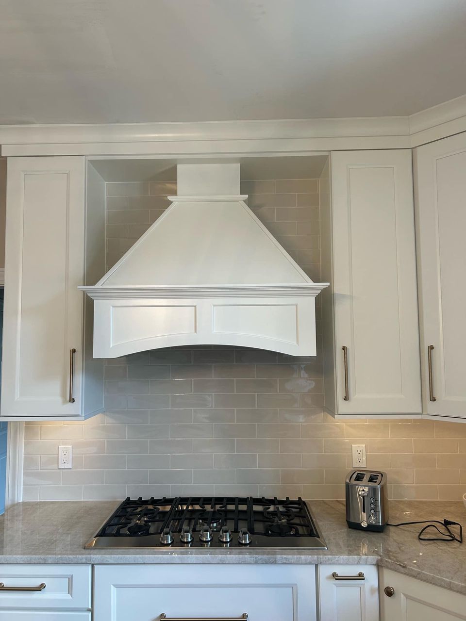 A white range hood centered between white kitchen cabinets above a gas stove with subway tile backsplash.