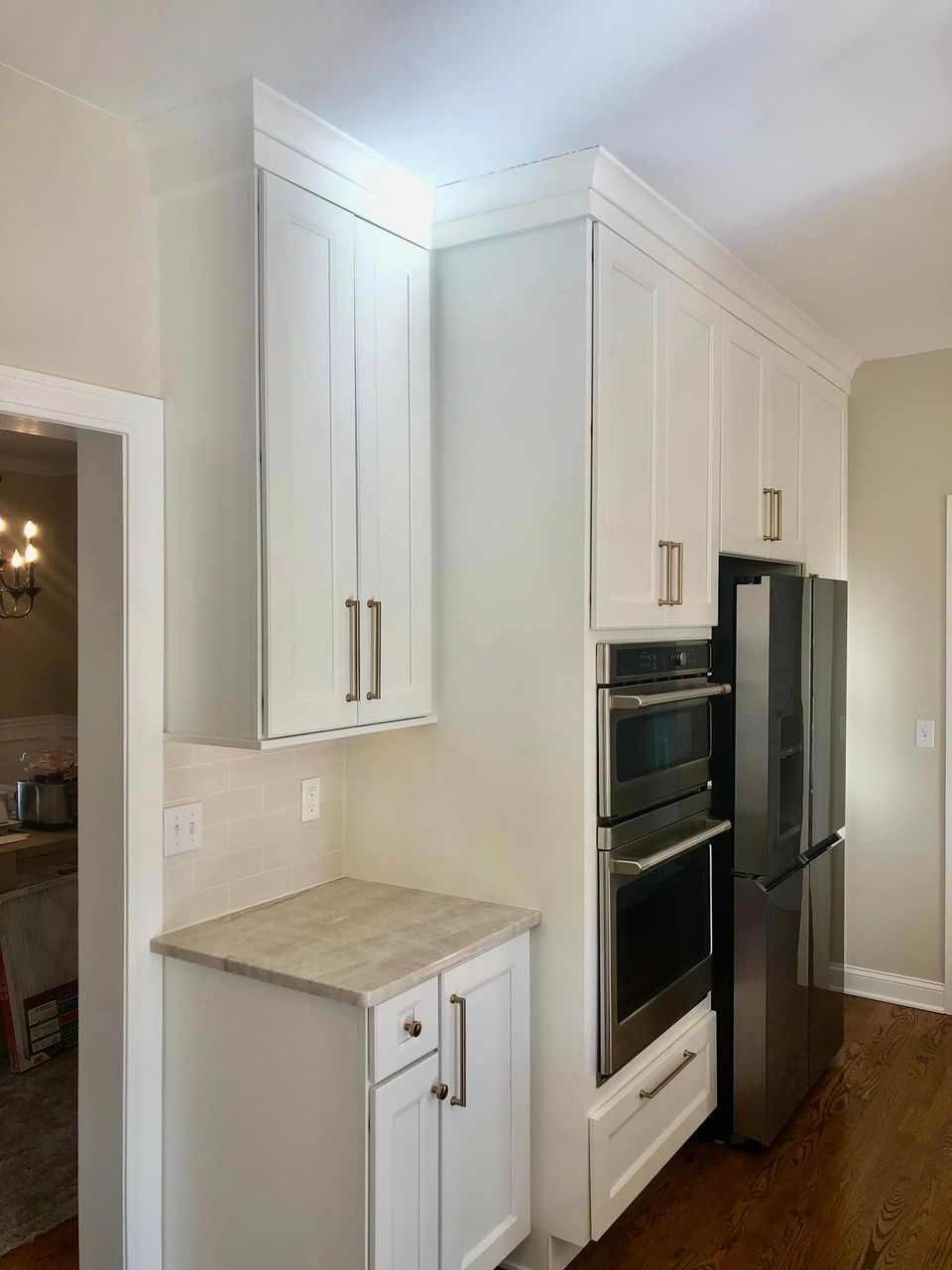 A kitchen area with white cabinetry, a light stone countertop, a built-in wall oven, and a stainless steel refrigerator.