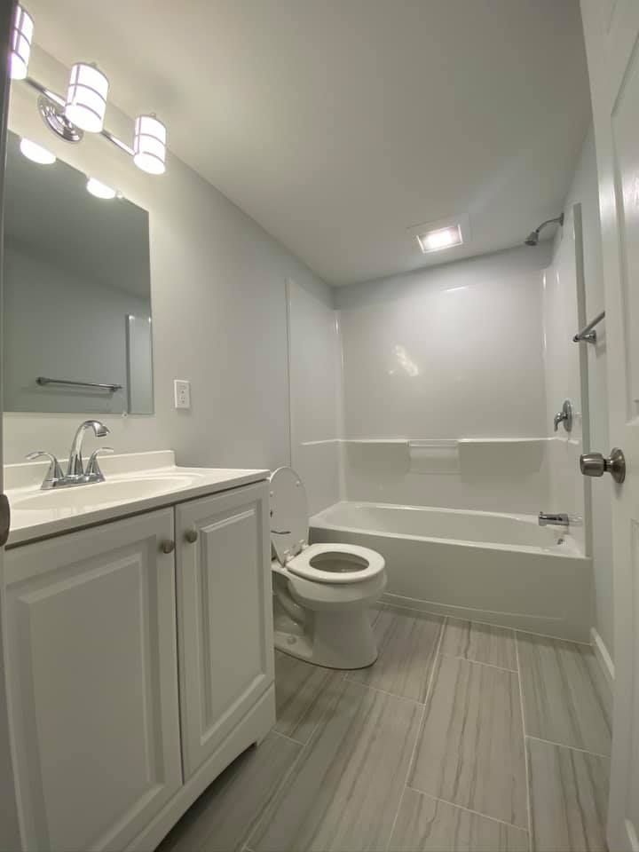 A bright bathroom featuring a white vanity with a silver faucet, a toilet, and a bathtub with white tiled walls.