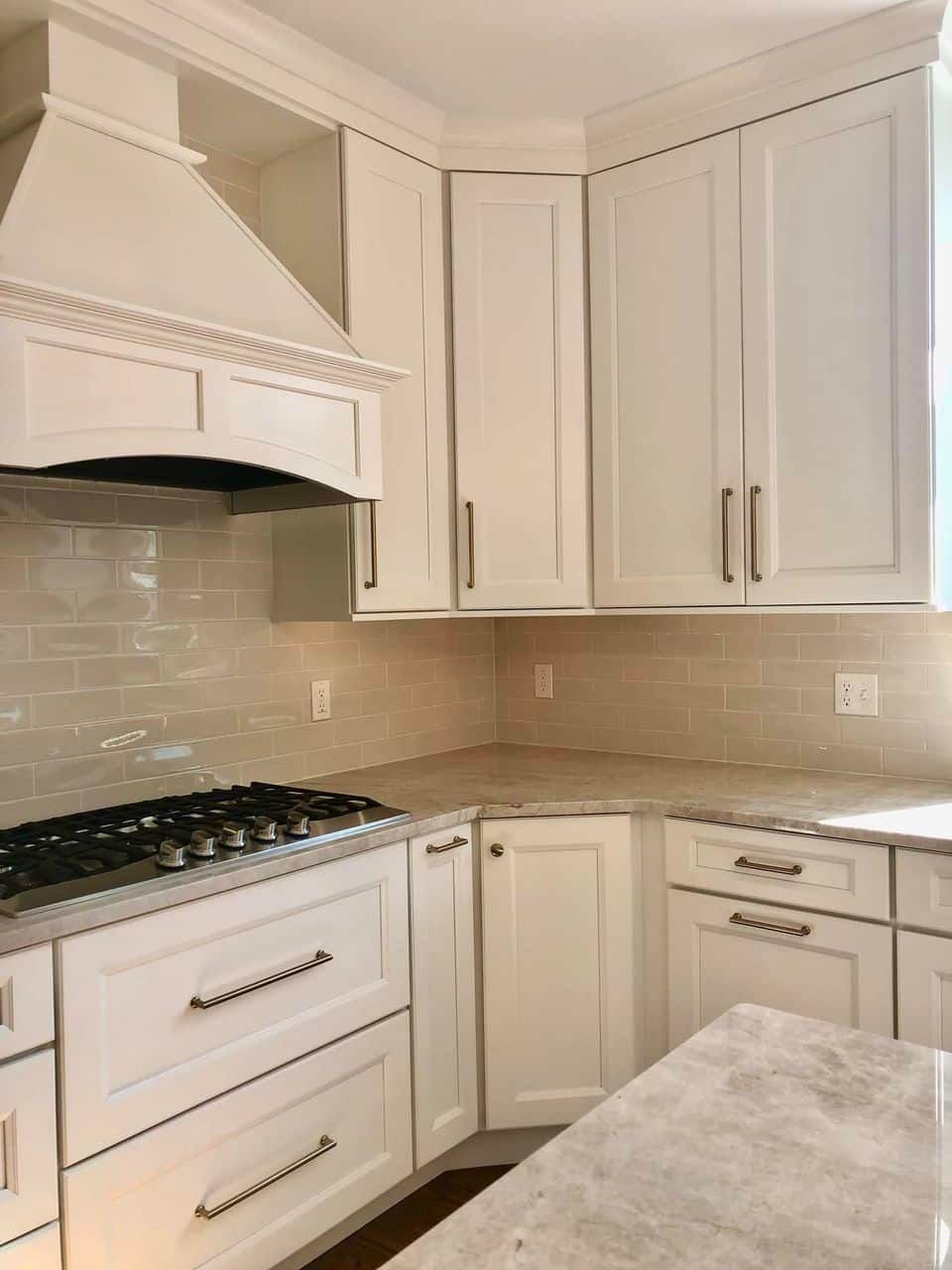 A modern kitchen corner featuring white shaker-style cabinets, a matching range hood, and a marble countertop.