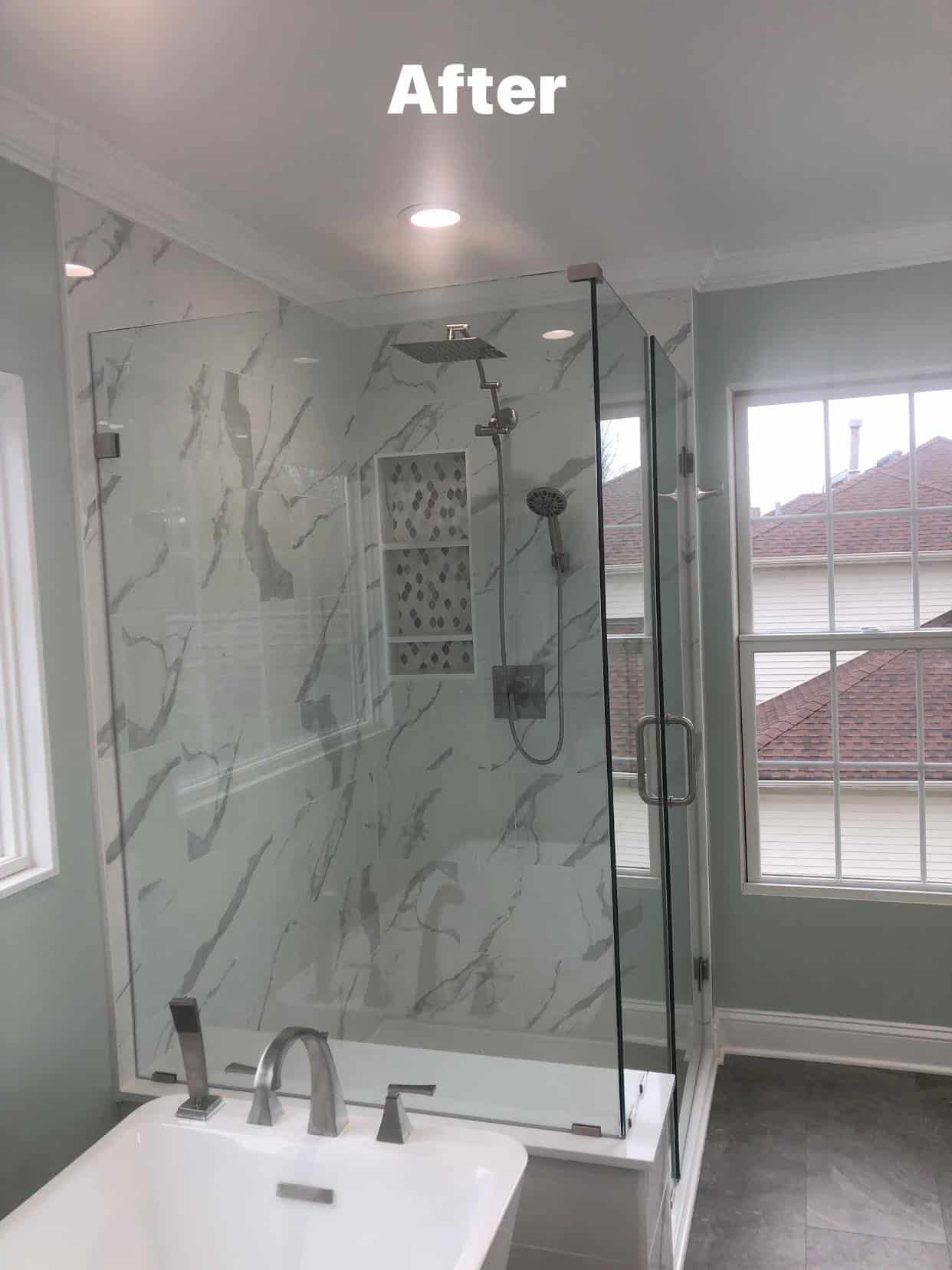 A renovated bathroom featuring a glass shower stall with white marble-patterned tiles and a white freestanding tub.