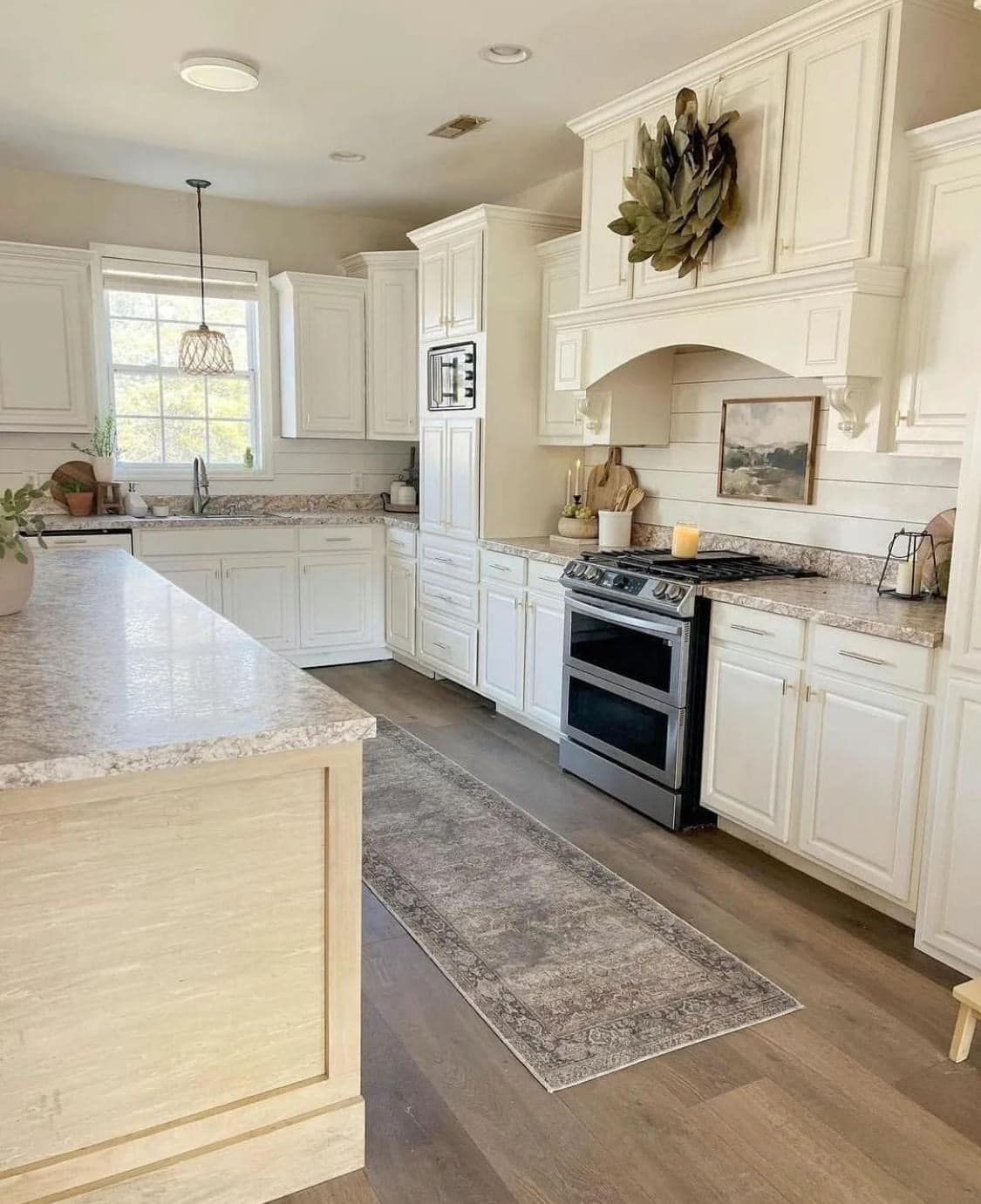A bright kitchen features white cabinets, a large island with light wood paneling, a stainless range, and a grey rug.