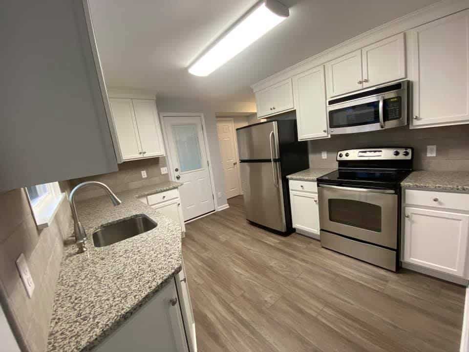 A kitchen with white cabinets, granite countertops, stainless steel appliances, and wood-look flooring.