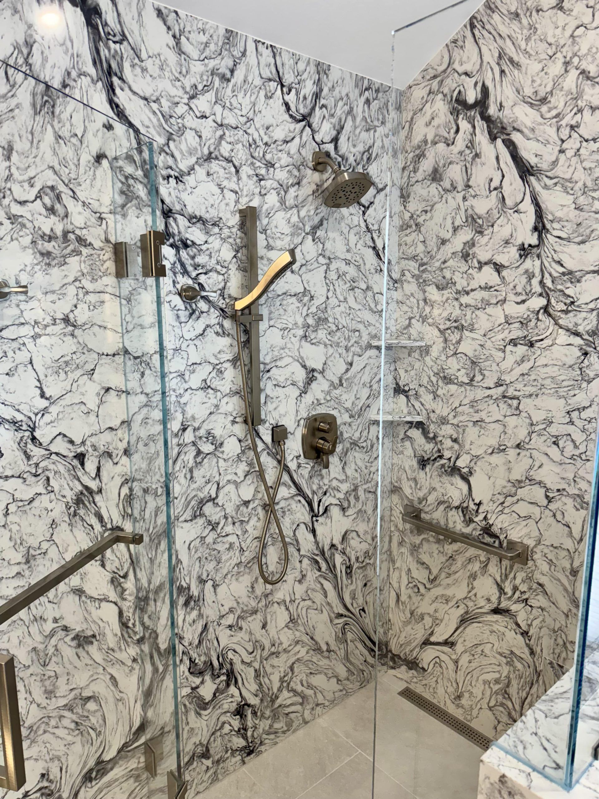 A walk-in shower with high-contrast, black-and-white marble walls and bronze fixtures behind a glass door.