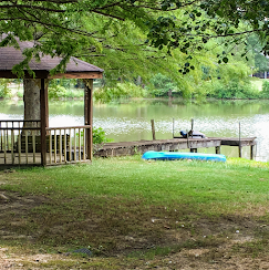 Gazebo by a grassy lakeshore with a blue kayak and dock under leafy trees