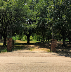 Tree-lined park entrance with brick pillars and open gates leading to a grassy path