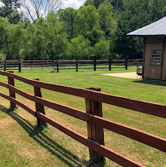 Red wooden fence beside a green pasture with trees and a barn on the right
