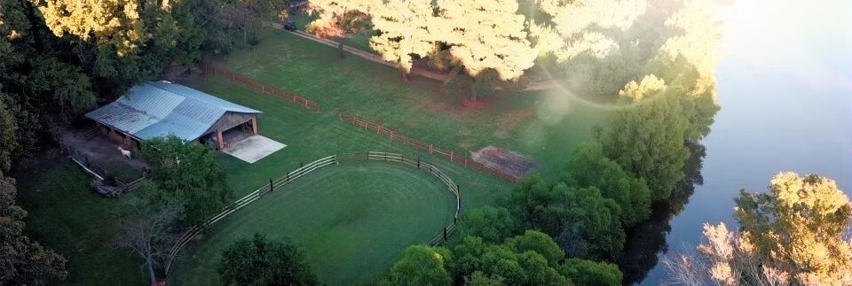 Aerial view of a green riverside park with a small pavilion and walking path beside the water