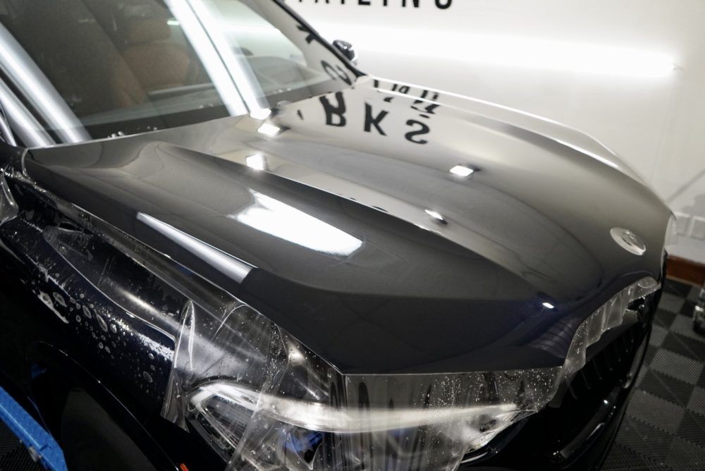 The hood of a black car is wrapped in plastic.