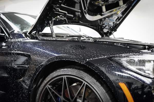 A black car with the hood open is sitting in a garage.