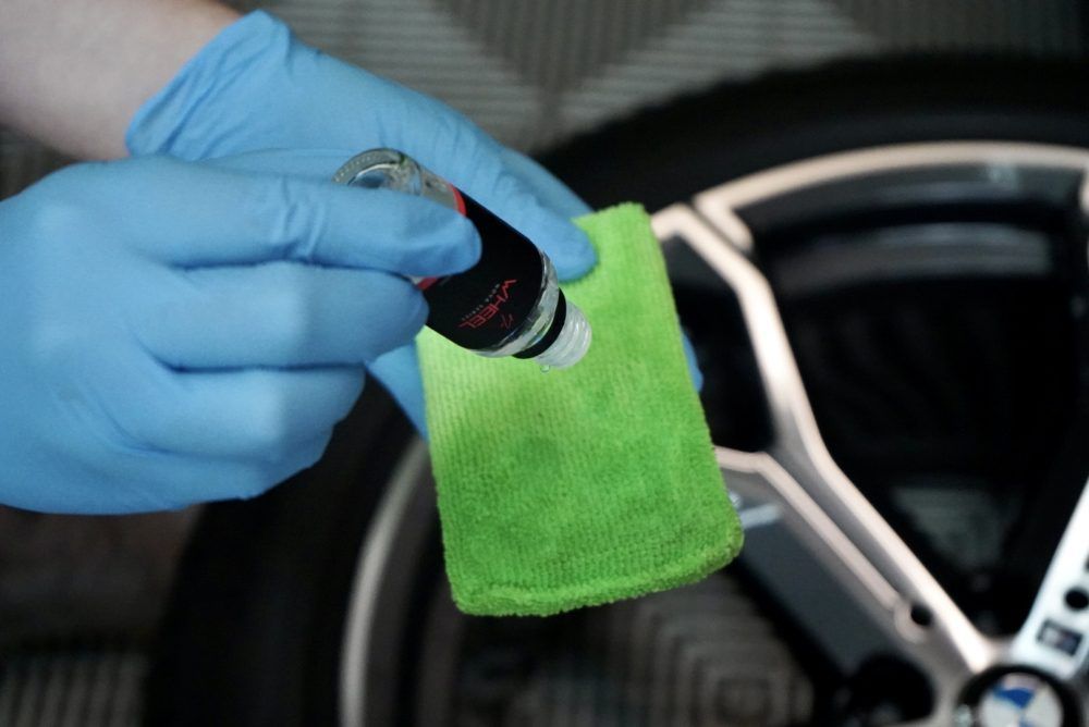 A person wearing blue gloves is cleaning a wheel with a green cloth.