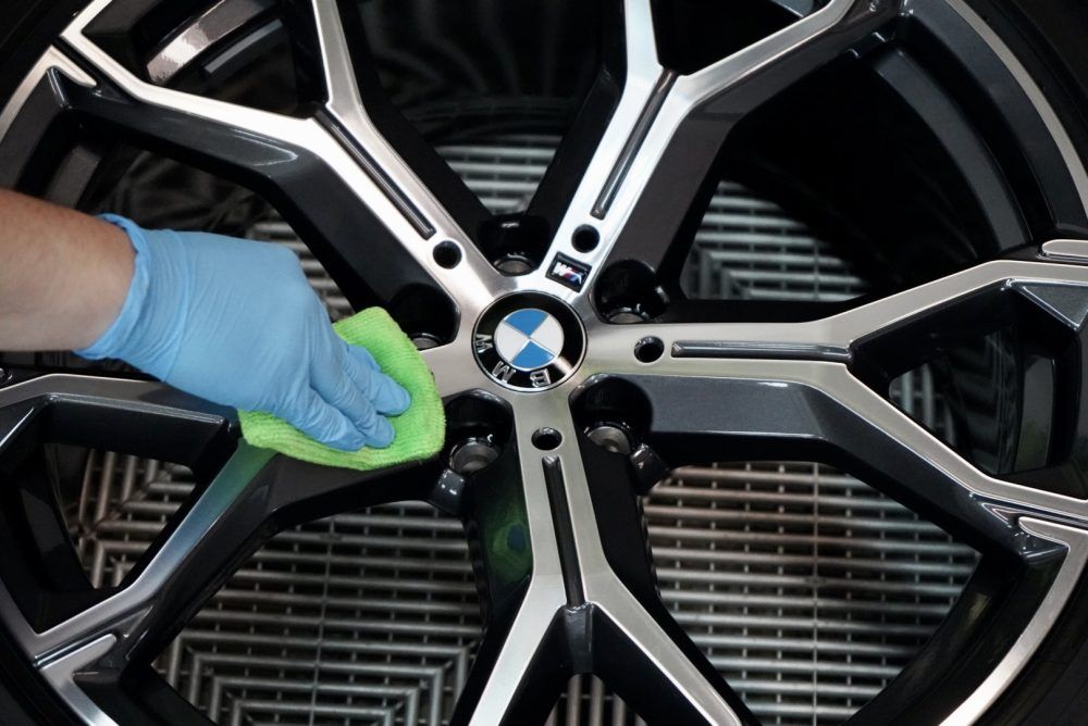 A person is cleaning a bmw wheel with a green cloth