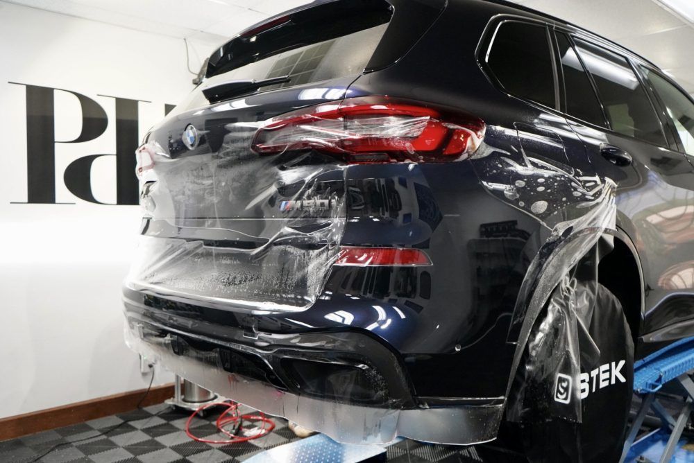 A bmw x5 is wrapped in plastic and sitting on a lift in a garage.