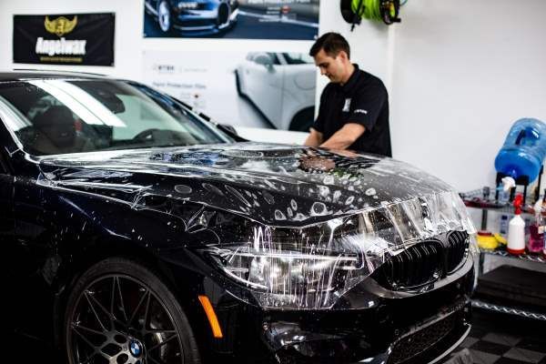 A man is covering the hood of a car with plastic wrap.