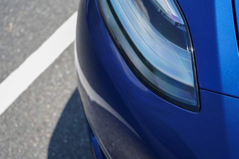 A close up of a blue car 's headlight in a parking lot.