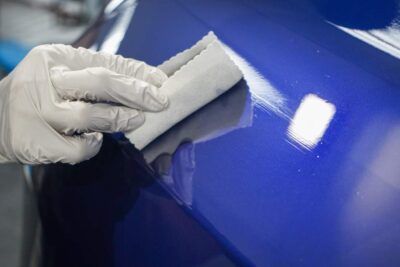 A person is polishing a blue car with a sponge.