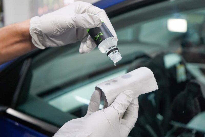A person is applying a coating to a car windshield.