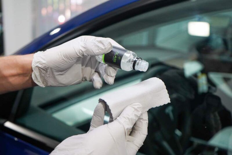 A person is cleaning a car windshield with a cloth and a spray bottle.