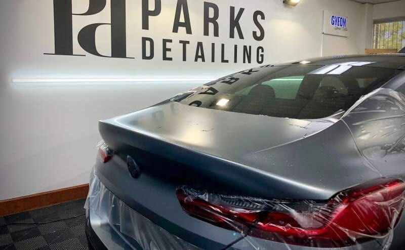 A car is wrapped in plastic and sitting in front of a sign that says parks detailing.