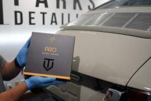 A person is holding a box in front of a car.