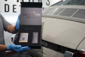 A man is holding a box in front of a car.