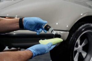 A person wearing blue gloves is applying a coating to a car.