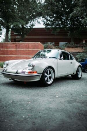 A white porsche 911 is parked in a parking lot in front of a building.