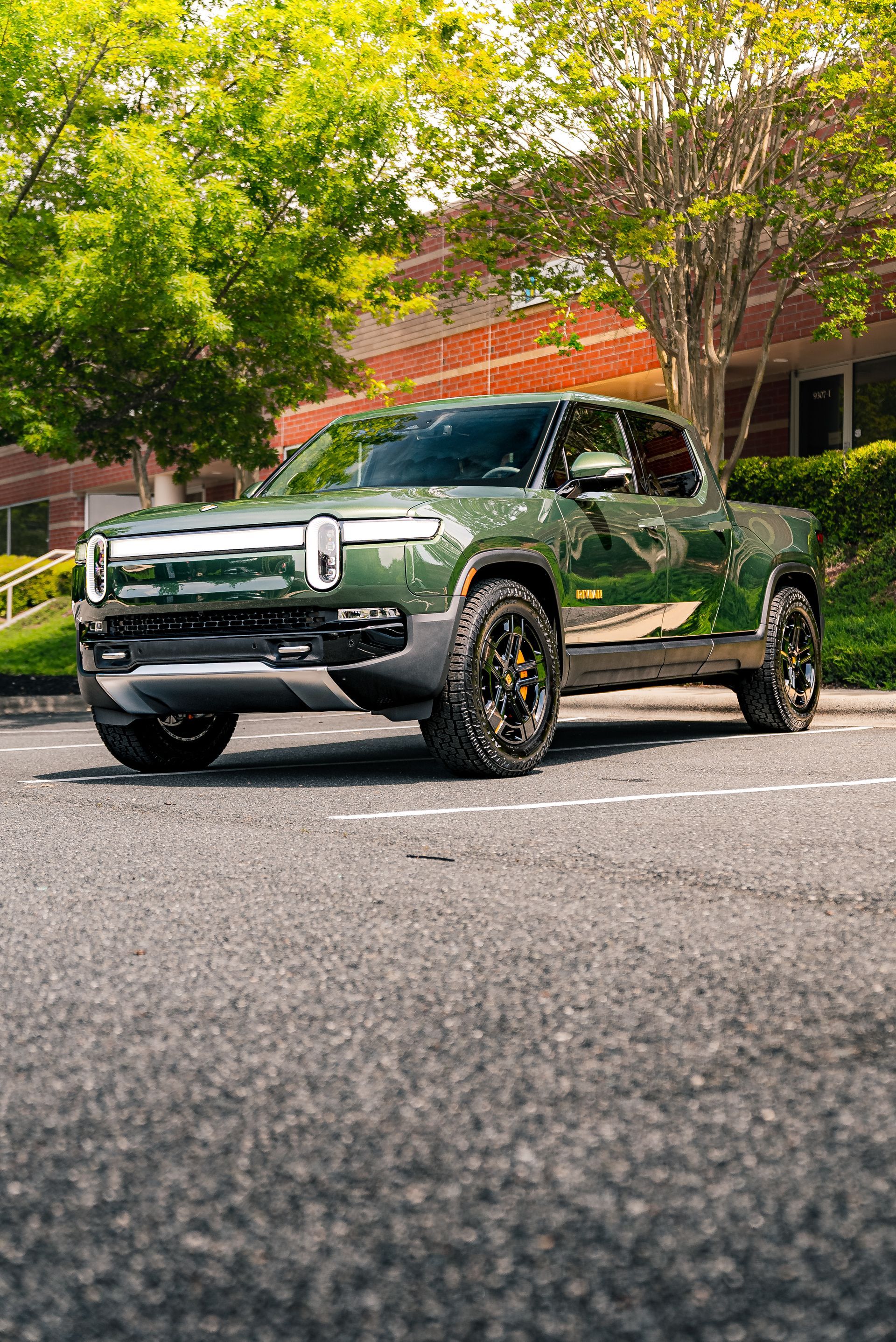 A green truck is parked in a parking lot in front of a building.