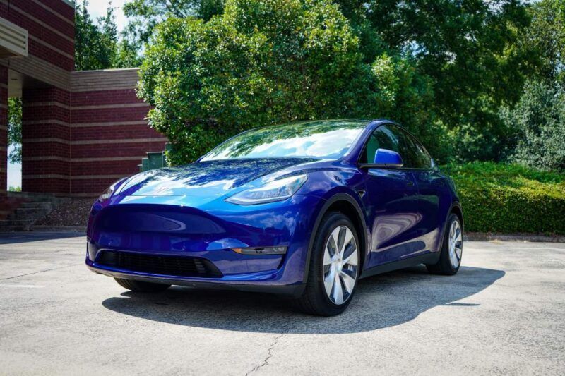 A blue tesla model y is parked in a parking lot in front of a building.