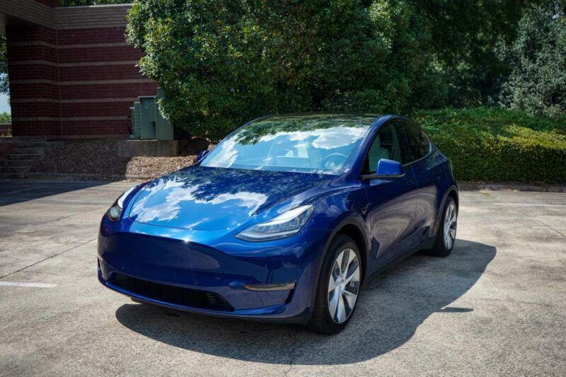 A blue tesla model y is parked in a parking lot.