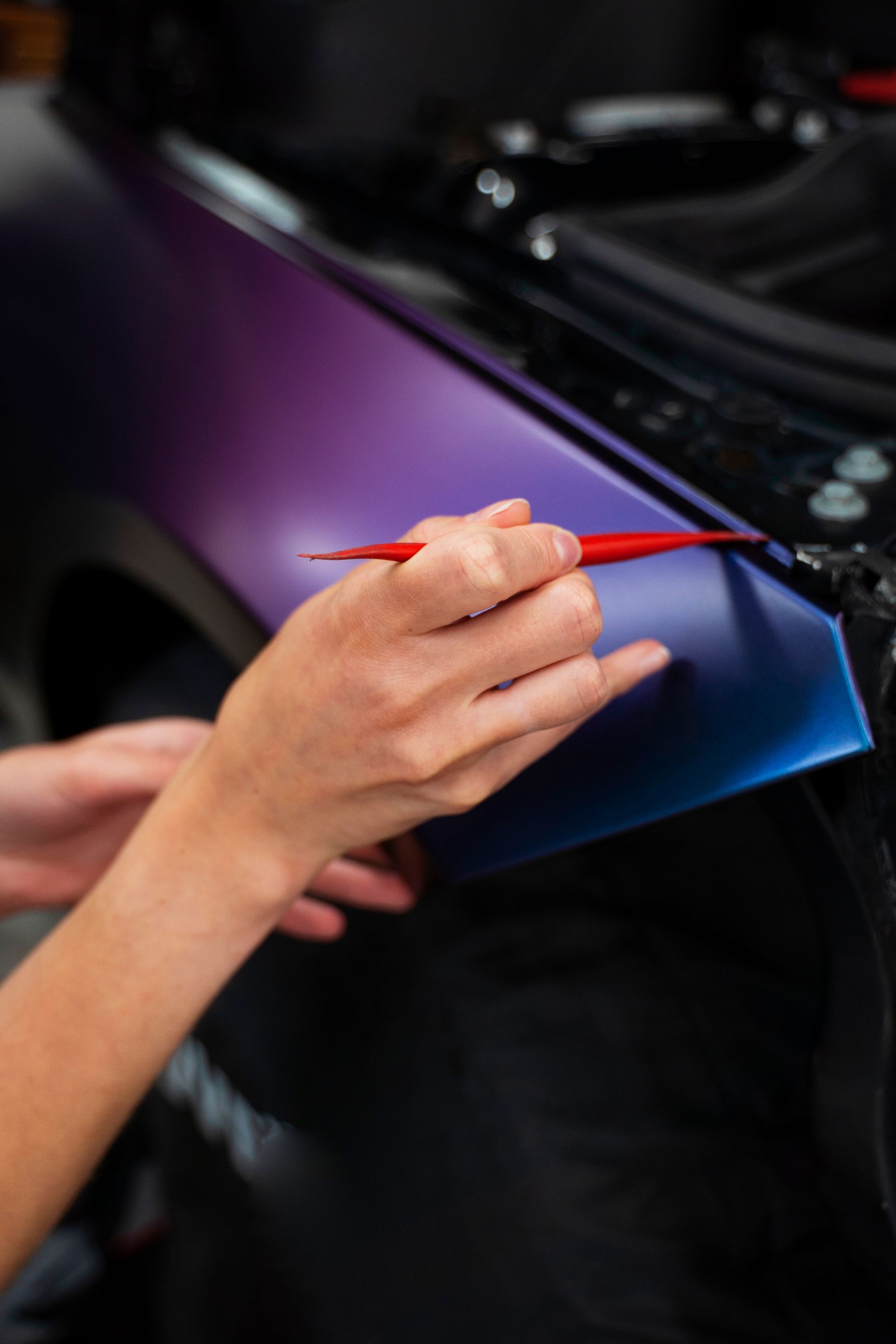 Two men are wrapping a car in plastic in a garage.