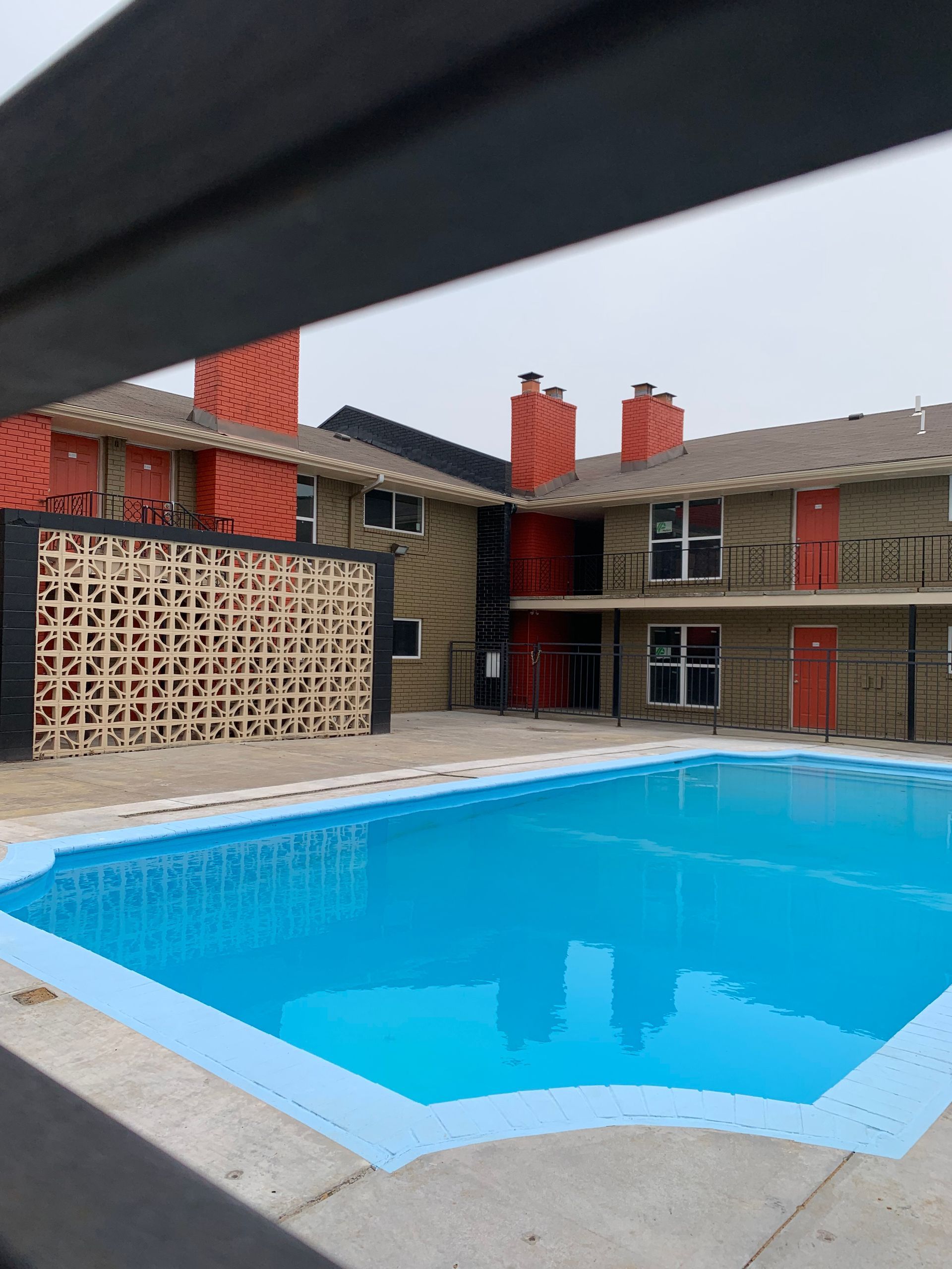 Apartment complex with a turquoise pool, red accents, and tan stucco walls.